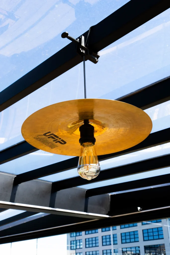 Piatto a rullante e lampadina a vista sotto la pergola in vetro di L.E.M., con vista sui palazzi di Milano