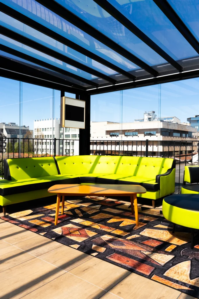 Lounge coperto di L.E.M. a Milano, con divano ad angolo verde e vista sui tetti della città